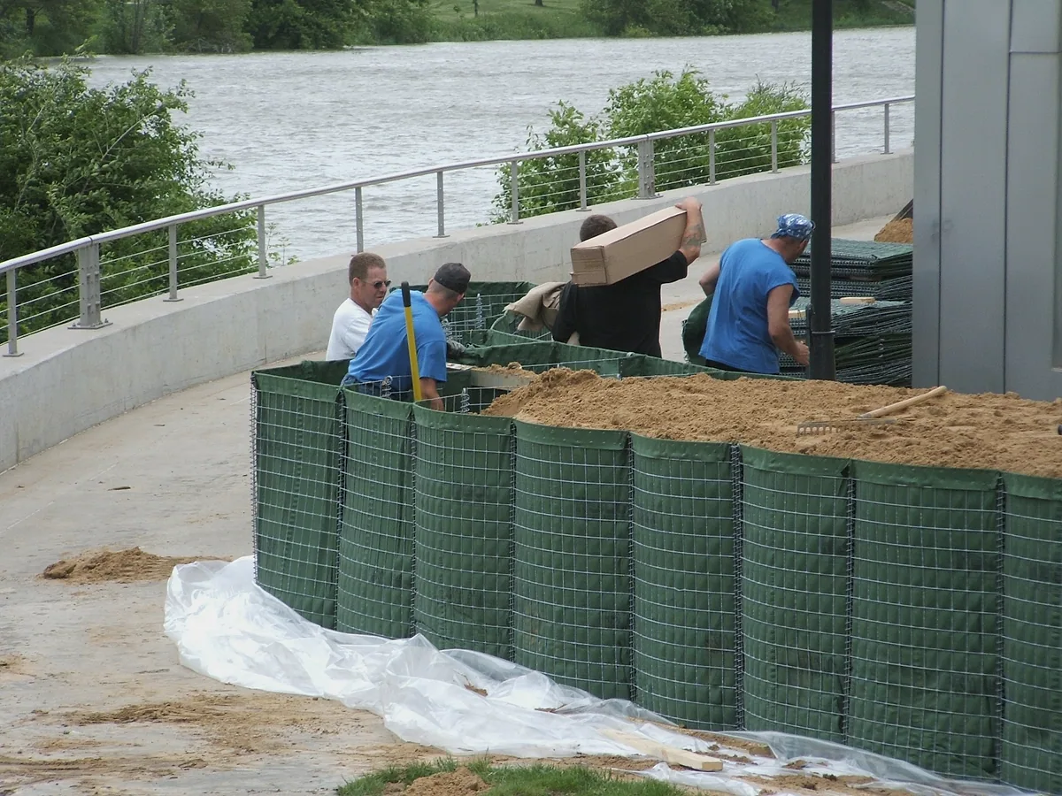 geotextile lined defensive barrier units being filled with sand for protective wall construction