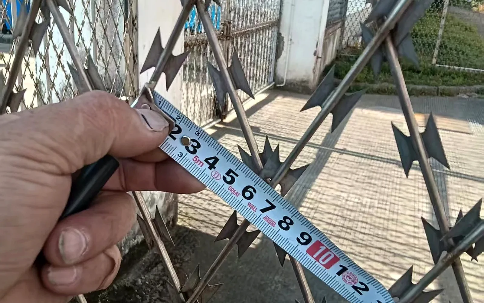 tape measure held beside razor wire loops for a spacing check
