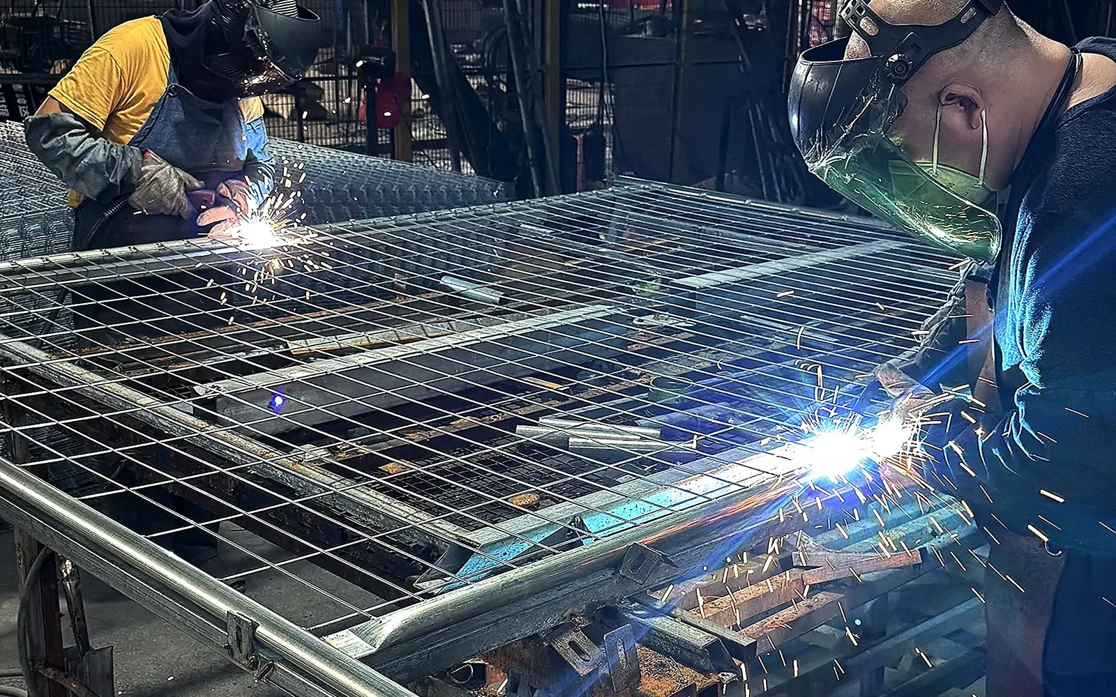 two workers welding framed wire mesh panels in a workshop